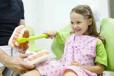 young patient practicing brushing teeth on a large model set of teeth